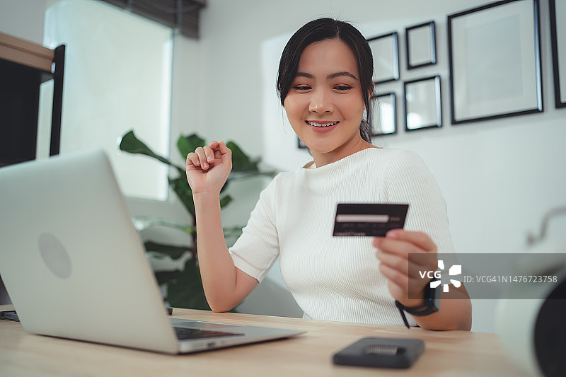 亚洲女性喜欢网上购物，持有信用卡，在家办公时使用笔记本电脑进行在线支付。图片素材