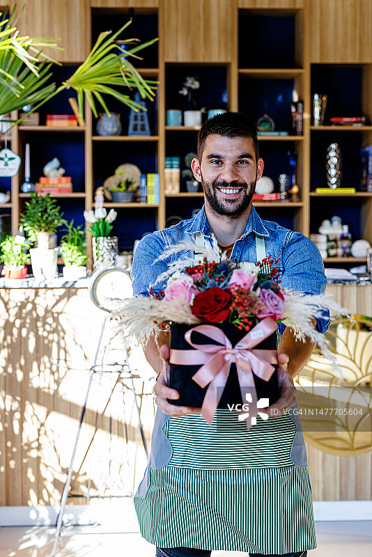 一位英俊的男子在一家现代花店里捧着鲜花。图片素材