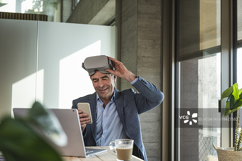 成熟的商人戴着VR眼镜在办公室使用智能手机图片素材