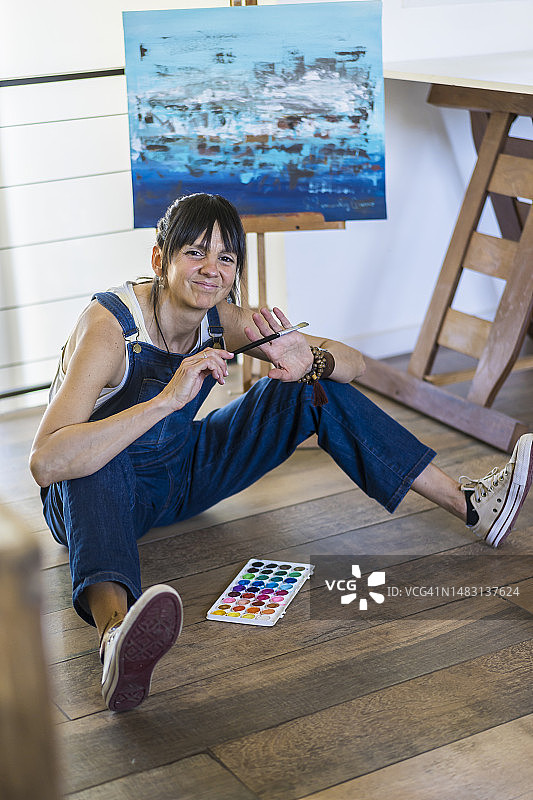 一位女艺术家坐在地板上看着相机的肖像。图片素材