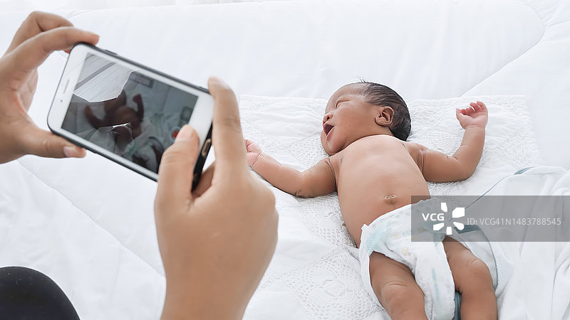 母亲用智能手机给新生儿拍照图片素材