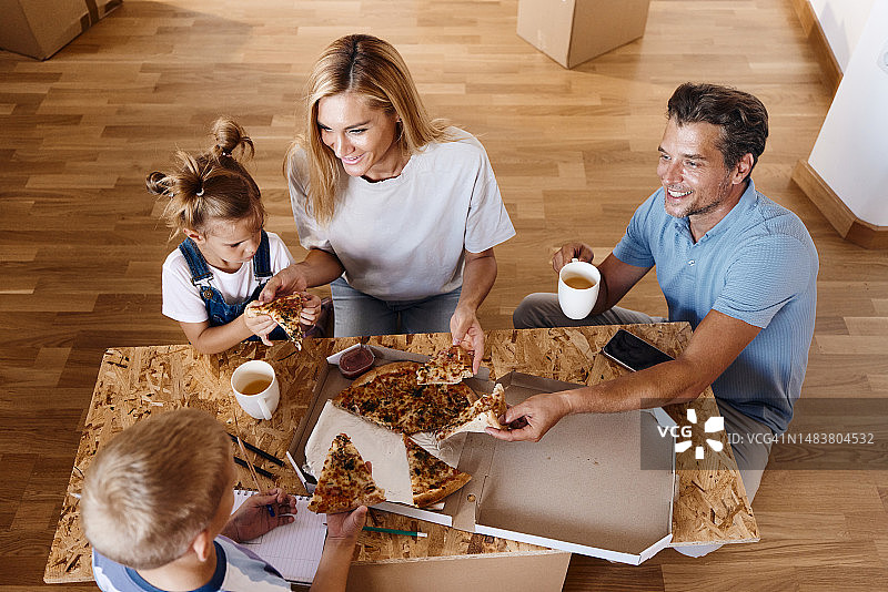 在新家打开行李后，一家人开心地吃着披萨。图片素材