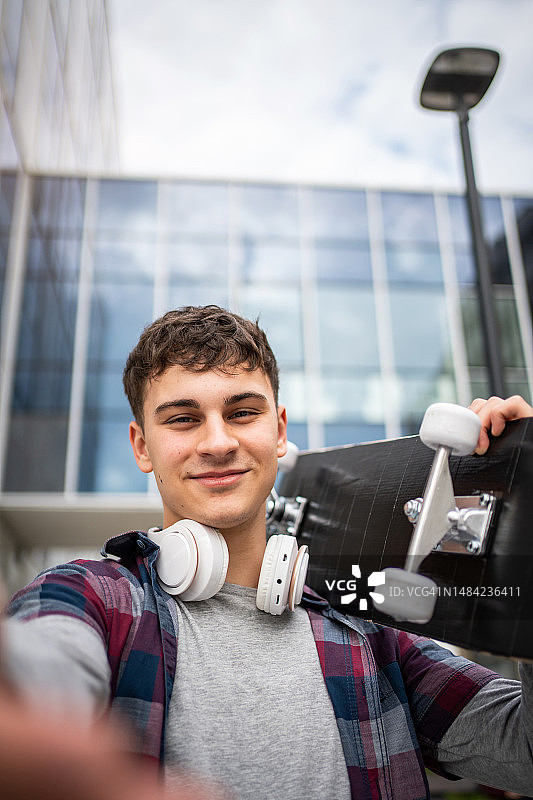 一名年轻人拿着滑板在外面自拍，发在社交媒体上图片素材
