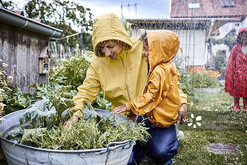 母亲和儿子穿着雨衣在花园里的花盆前图片素材
