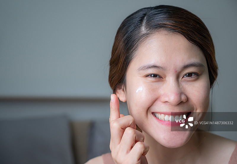 一名亚洲妇女在脸上涂面霜治疗痤疮和皮肤发红。图片素材