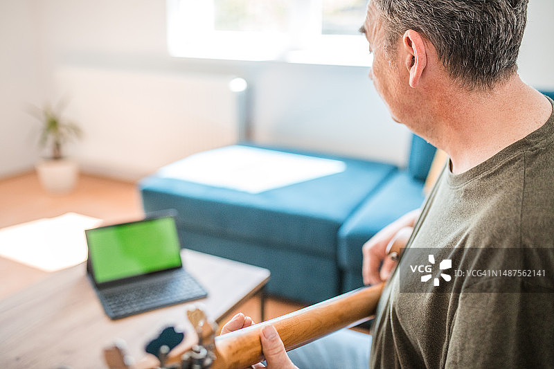 男吉他手在客厅里弹吉他，看着绿屏的数码平板电脑图片素材