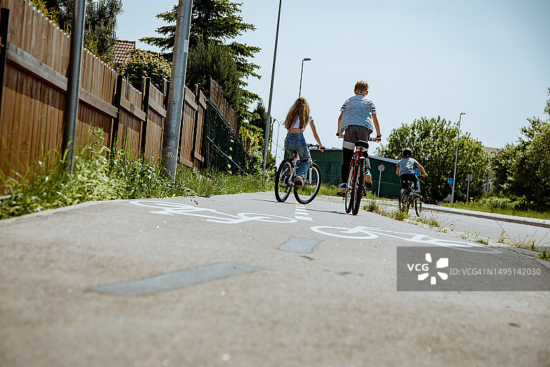 一小群孩子沿着郊区的自行车道骑行的后视图图片素材