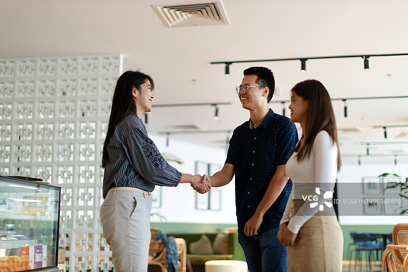 在一家现代化的自助餐厅里，一名亚洲女商人正在与新客户握手，庆祝成功达成协议图片素材