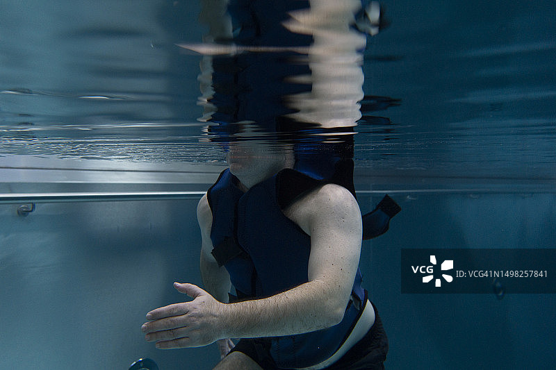 一位穿着漂浮背心的病人在游泳池里做物理治疗图片素材