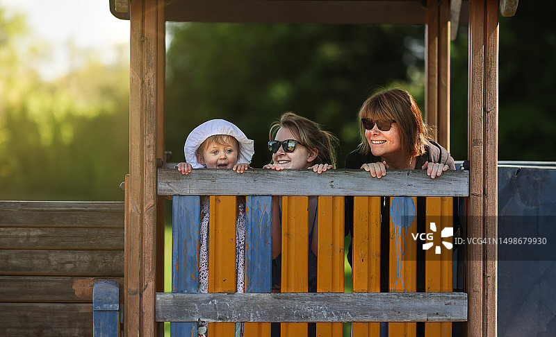 三代人在公园里玩耍。外孙女、母亲和祖母微笑着，透过木制的火车护栏一起玩耍图片素材