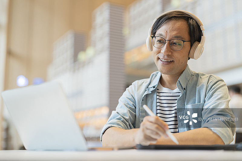 聪明自信亚洲创业企业家企业主商人微笑使用笔记本电脑上网工作听音乐无线耳机工作放松休闲在咖啡馆图片素材