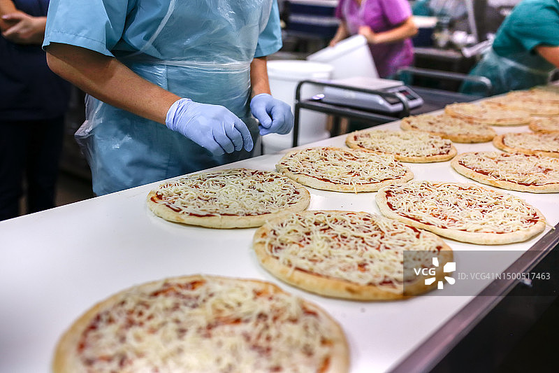 奶酪在食品输送生产线上的应用:披萨装配线上熟练工人的双手图片素材