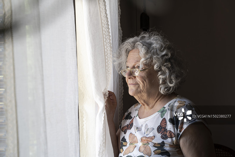 她是一位上了年纪的妇女，一边等着什么东西，一边望着窗外图片素材