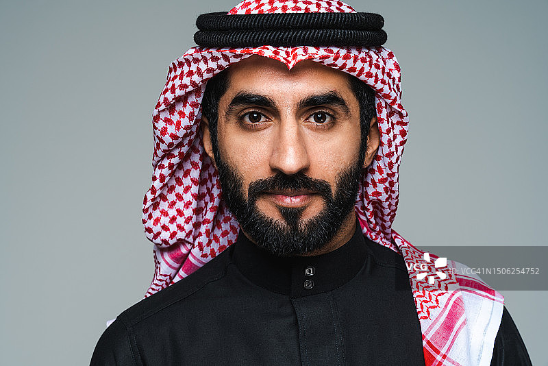 英俊的沙特阿拉伯中东男子与传统的thwab肖像在工作室对灰色背景，阿拉伯联合酋长国图片素材