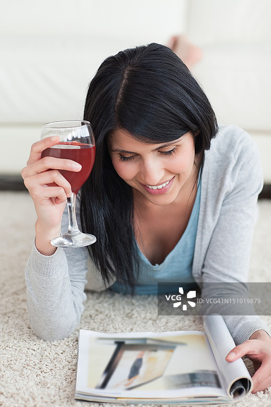一个女人拿着一杯酒，微笑着看地上的杂志图片素材