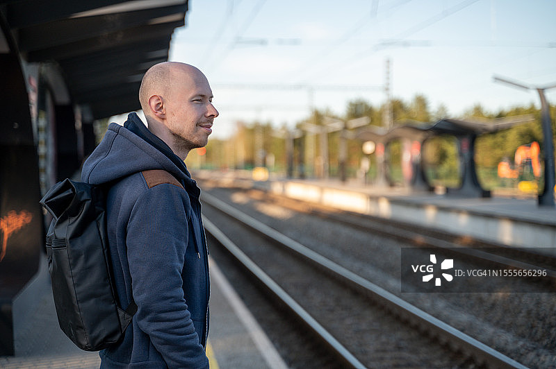 一个秃头男人站在站台上，望着前方，等着火车图片素材