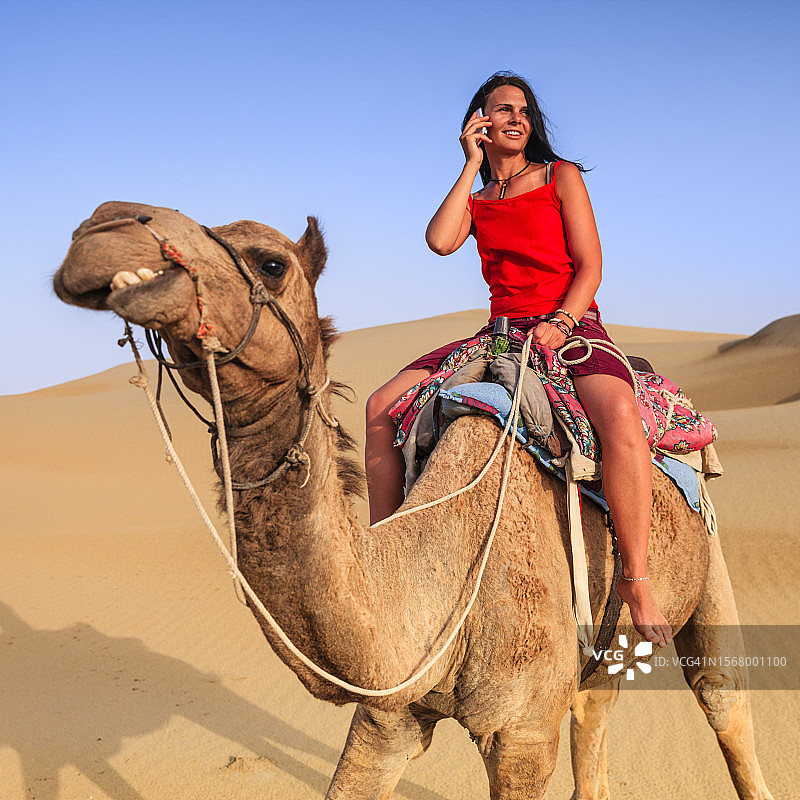 印度拉贾斯坦邦，年轻女游客骑着骆驼使用手机图片素材