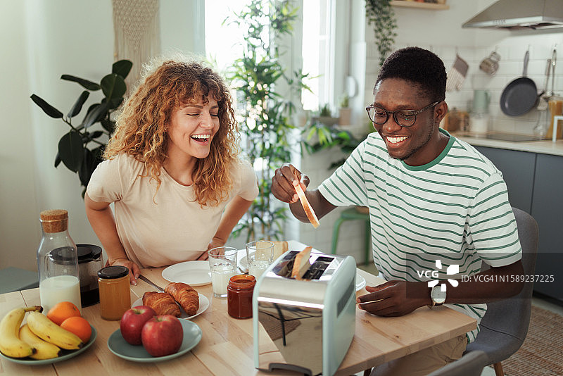 微笑的年轻夫妇在厨房一起吃早餐图片素材