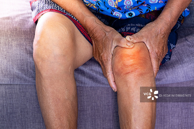 老年妇女在家里客厅沙发上抱着疼痛的膝盖。老的年龄。她的症状是双膝疼痛，由于骨质疏松，到退休年龄和保健观念。图片素材