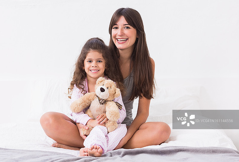 妈妈和女儿和泰迪熊坐在床上图片素材