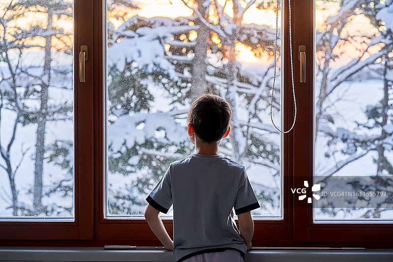 男孩站在窗前，看着冬天的风景。图片素材