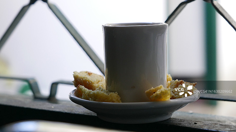 窗边的热咖啡杯。一个小咖啡杯和一个玉米蛋糕盘。咖啡休息时间:一杯黑咖啡。窗边的咖啡杯。一杯咖啡放在蛋糕盘上。黑咖啡，侧视图，特写图片素材