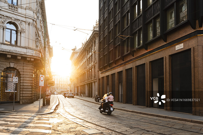 在意大利米兰的街道上，摩托车在日落时行驶图片素材