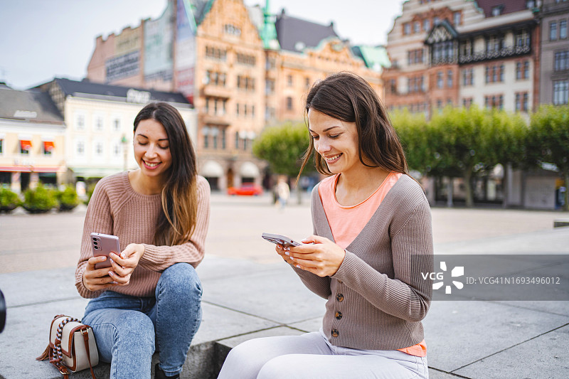 两名女游客在城市广场的台阶上玩手机图片素材