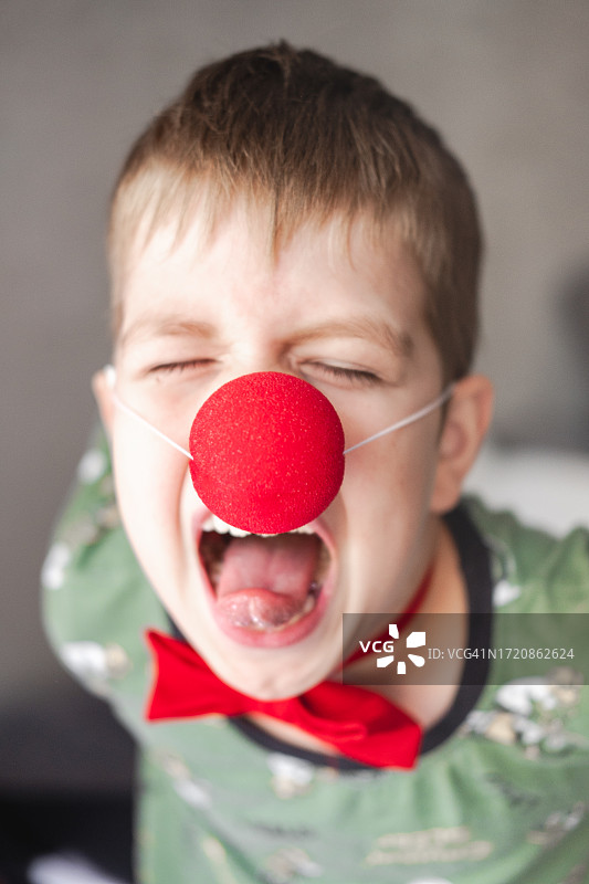一个长着小丑鼻子和突出舌头的9岁男孩的肖像。孩子强烈的情感。顽皮的男孩图片素材