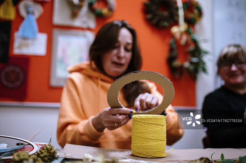 在艺术治疗课的创意拥抱中，巧妇将黄绳缠绕在纸板圈上，将剪纸变成迷人的装饰底座图片素材