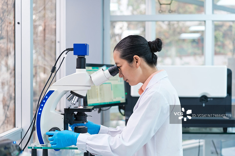 女科学家在实验室通过显微镜观察的侧视图图片素材