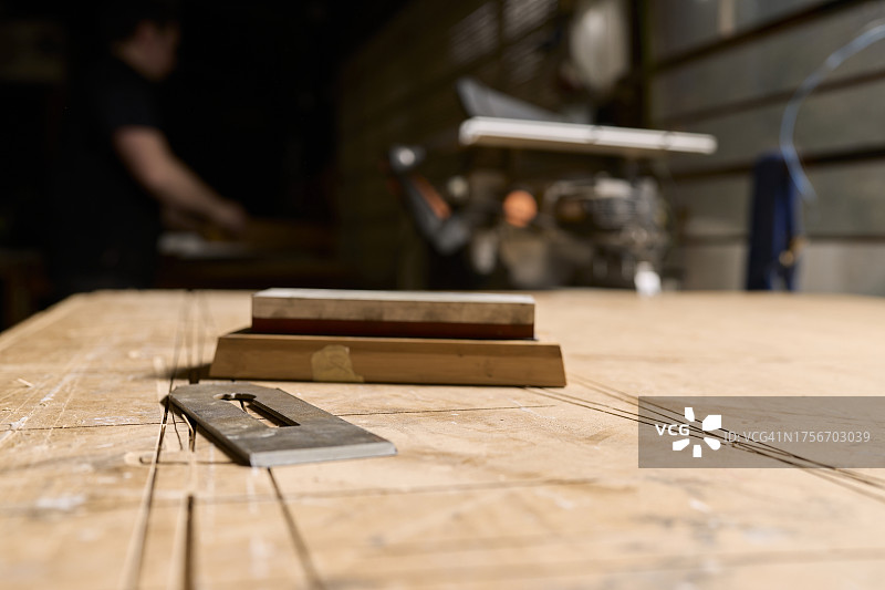 背景中木制工作台上一把木匠的刨刀是一个男人的身影。图片素材