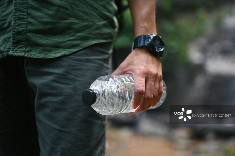 一名男性旅行者拿着一瓶水，背景是模糊的森林图片素材