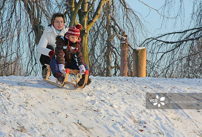 滑雪橇的乐趣——母亲和女儿滑雪橇下山图片素材