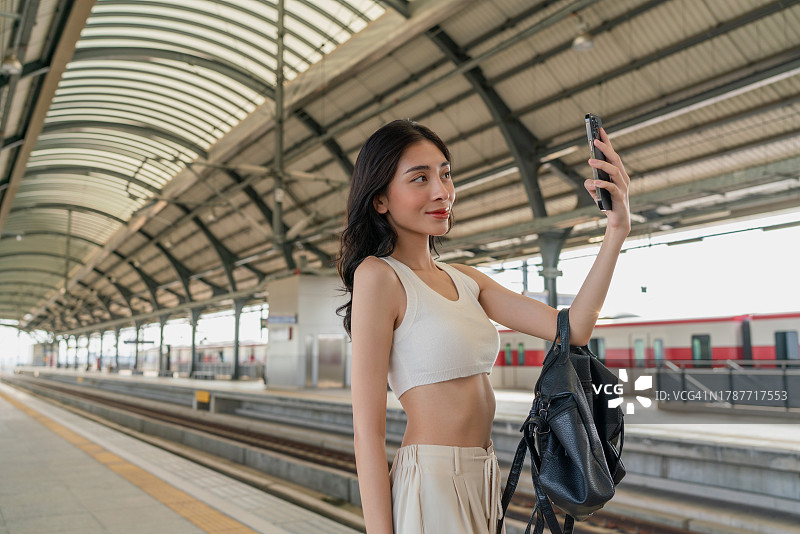 年轻的亚洲女子在地铁站台用手机自拍。无处不在的数字银行。商业在移动。年轻的亚洲女商人放松周末旅行。图片素材