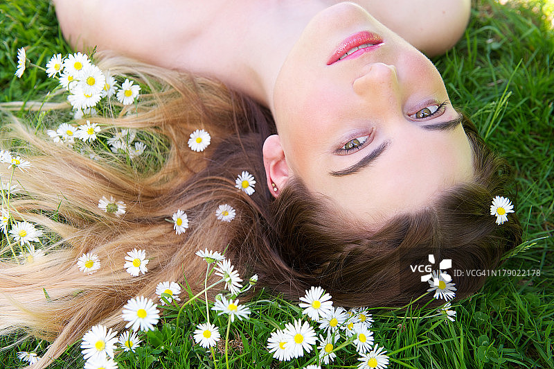 年轻女子躺在户外的草地和鲜花上图片素材