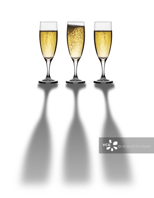 三个装满香槟的酒杯，白色背景上有长长的阴影。图片素材
