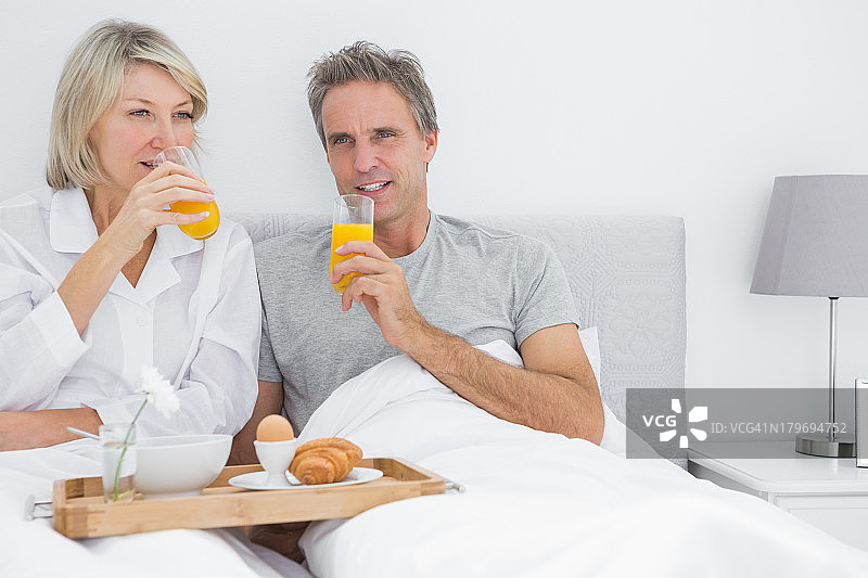 一对夫妇在床上喝橙汁吃早餐图片素材