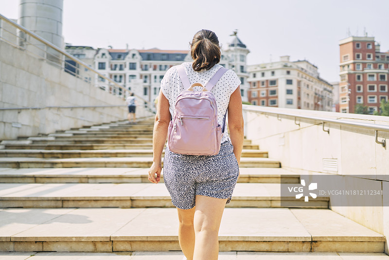 一名穿着便服背着背包的女游客站在一栋建筑外的楼梯上(后视图)图片素材