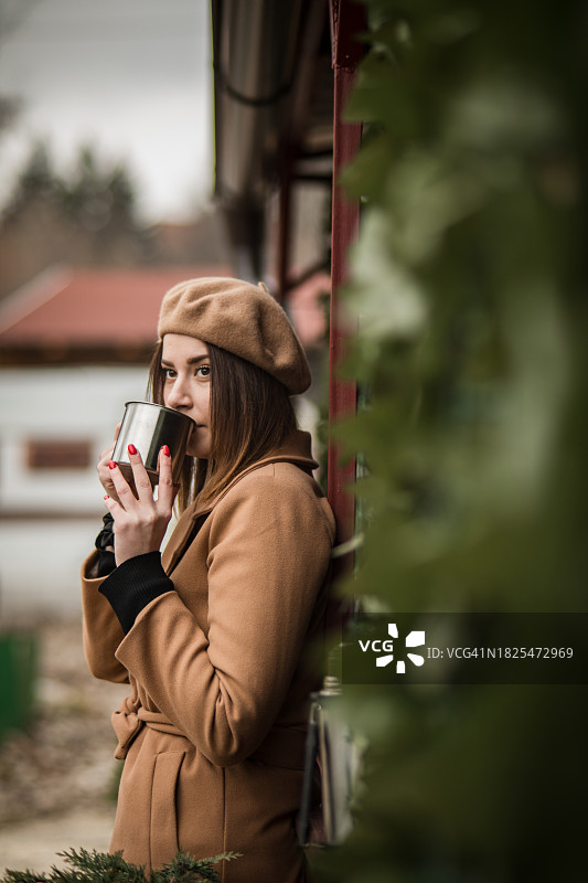 一个美丽的女人站在一个小木屋旁边，在大自然中，喝着热茶或咖啡，享受冬日的一天图片素材