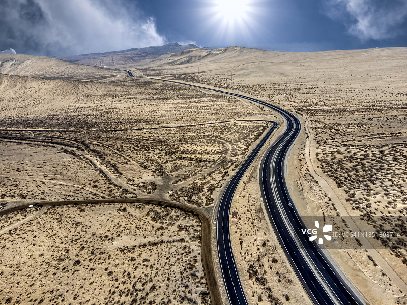 鸟瞰图，公路穿过沙漠景观的沙丘与太阳的光线上升在地平线上。图片素材