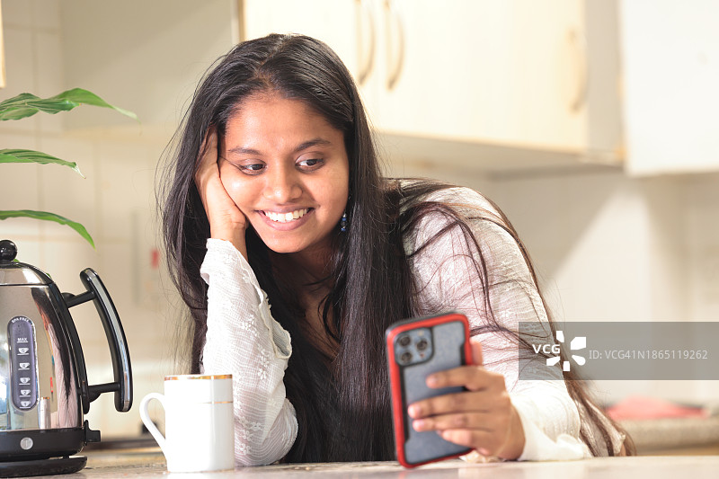 开心的亚洲女人在厨房看手机图片素材