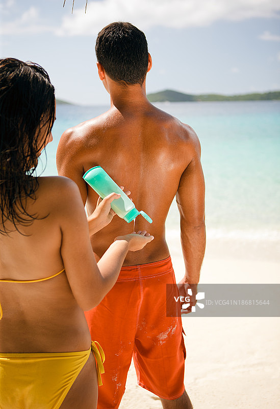 一个女人在海滩上给一个男人擦润肤水图片素材