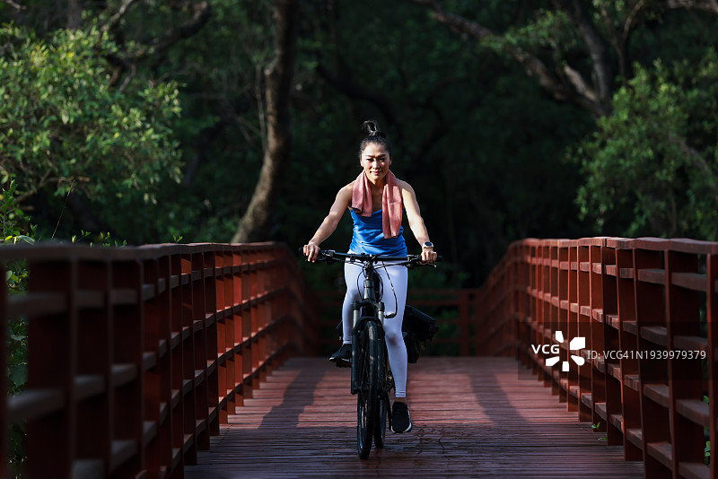 美丽强壮的女人在公园的木桥上骑自行车。一位穿着运动服的女士在大自然中骑自行车。积极有趣的生活方式。图片素材