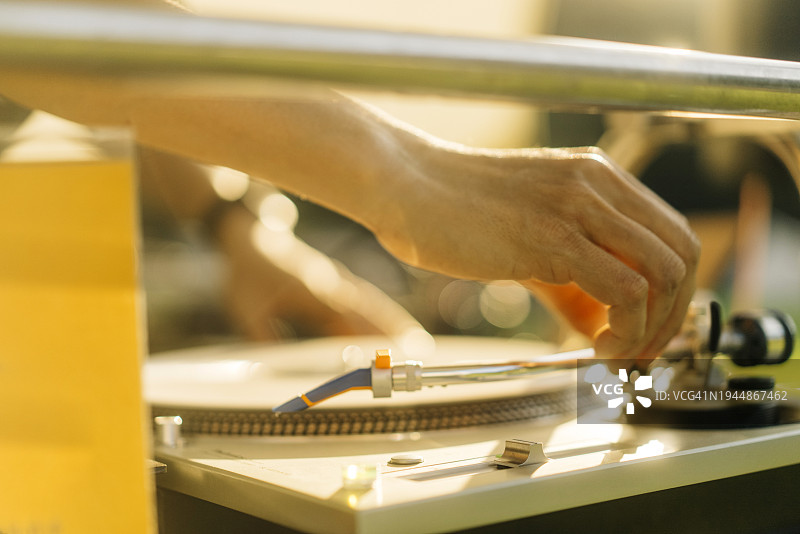 在阳光明媚的户外音乐活动中，DJ的手在转盘上微调设置的特写。图片素材