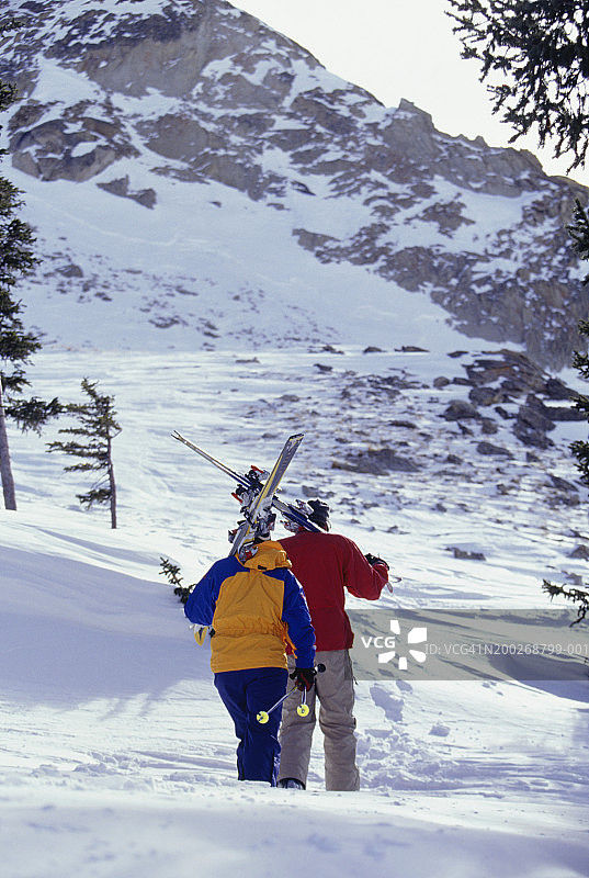 夫妇带着滑雪板爬上白雪覆盖的斜坡，后视镜图片素材