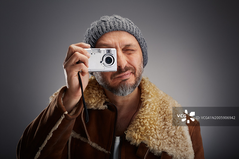 一名男子身穿皮大衣，头戴针织帽，拿着他的旧数码相机拍照图片素材
