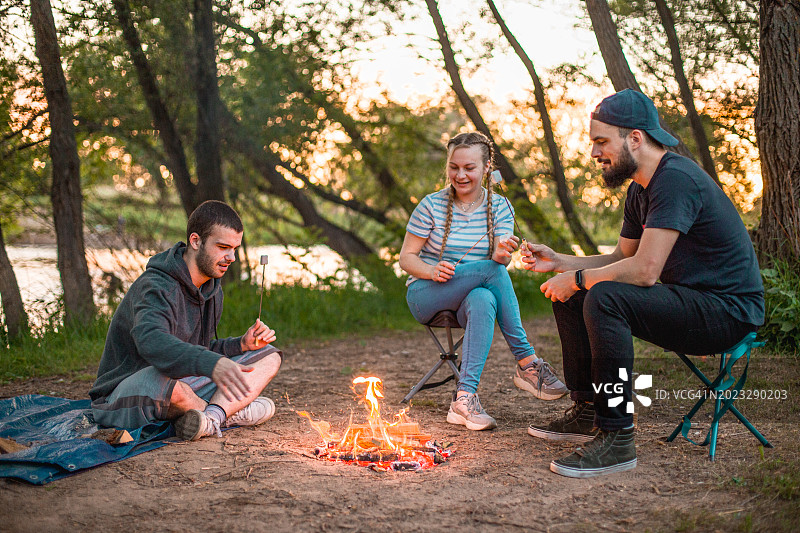 年轻的朋友们在户外玩耍，他们围坐在篝火旁烤棉花糖图片素材