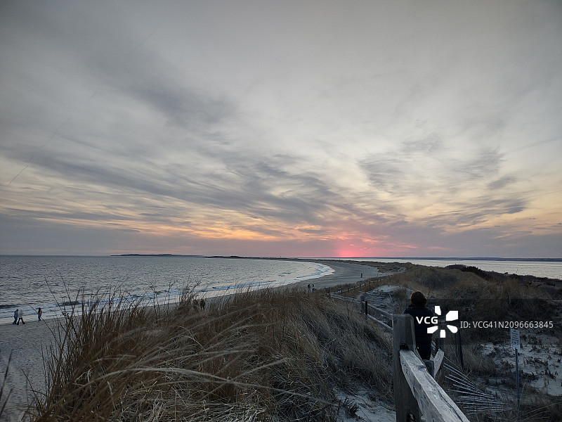 夕阳西下，美国罗德岛，一名女子走在沙滩上的沙丘上图片素材