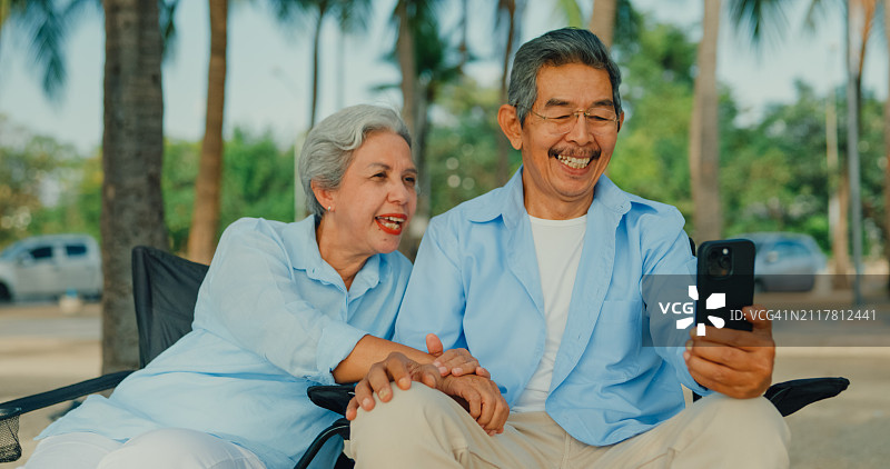 快乐的亚洲老夫妇微笑着用智能手机与度假的家人视频通话。一个快乐的老年人享受退休后的旅行生活方式。图片素材